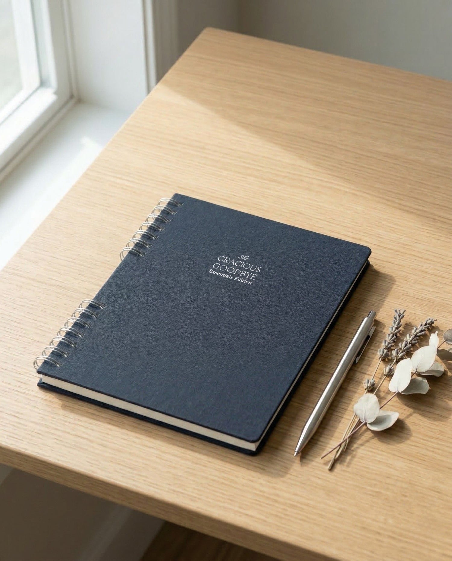 Blue Gracious Goodbye Essentials notebook with a pen and decorative elements on a wooden surface