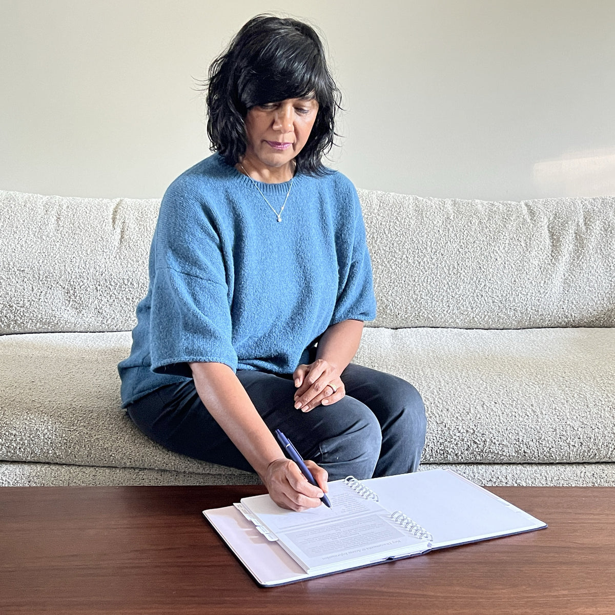 A woman sitting at a coffee table writing in The Gracious Goodbye Essentials.