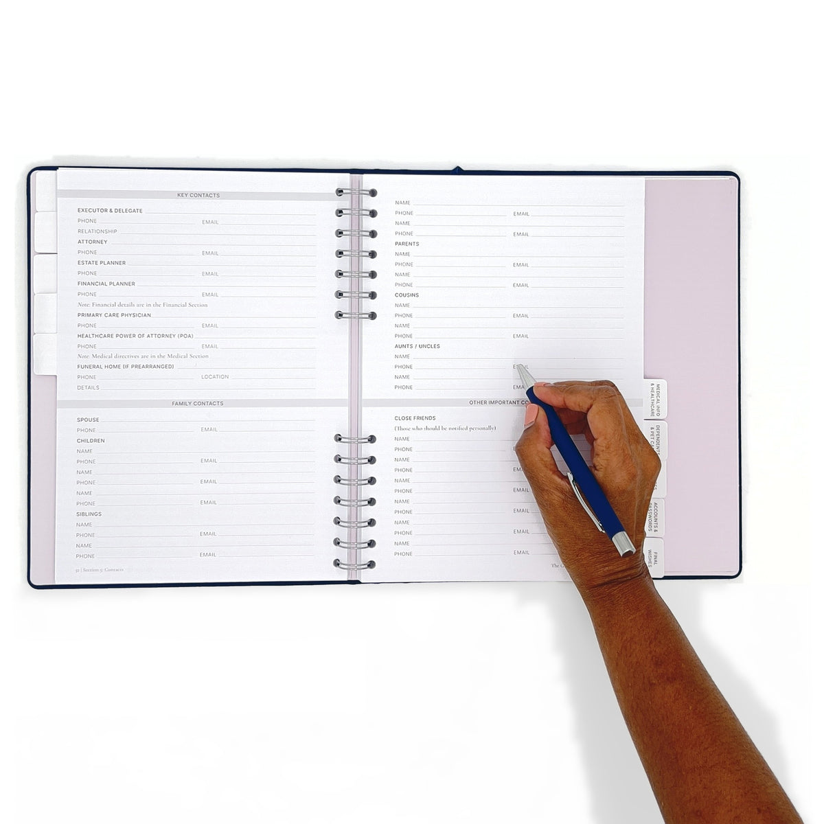 The Gracious Goodbye Essentials open flat at 180 degrees with a hand writing on the right page, the concealed spiral visible at the gutter.