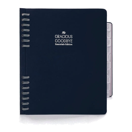 The Gracious Goodbye Essentials planner in navy linen, closed, with its silver-foil title, half-hidden spiral and section tabs along the edge.
