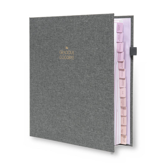 The Gracious Goodbye end-of-life planner in gray linen, standing closed, with its gold-foil title and labeled section tabs along the edge.