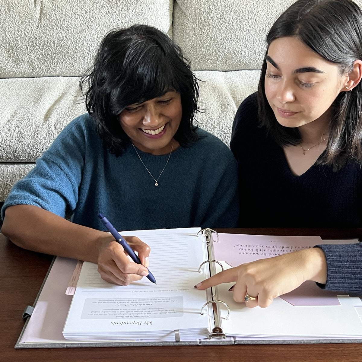 Two women at a coffee table working through The Gracious Goodbye planner together, one writing while the other points to the page.